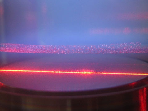 Лабораторный снимок пылевой плазмы. Здесь от неё исходит голубоватое свечение, а красный луч — это лазер, в котором хорошо заметны пылевые частицы (фото с сайта mpe.mpg.de).